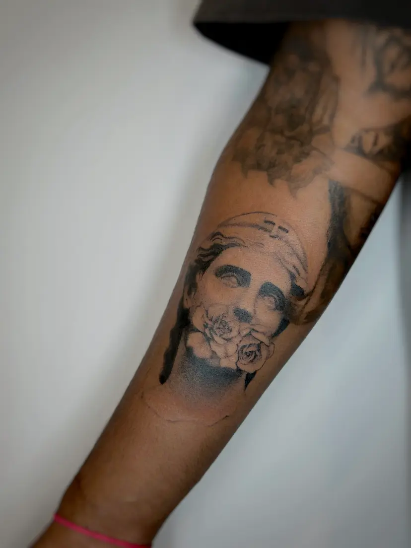 Black and grey statue face and rose tattoo on a forearm
