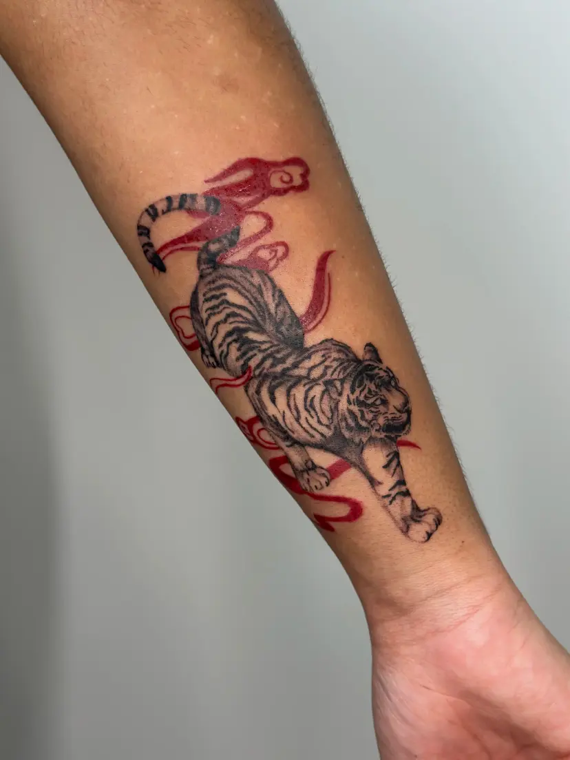 Tiger tattoo with red clouds on a forearm