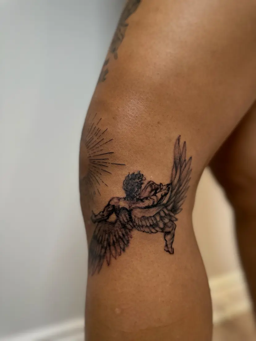 Winged figure falling from a sunburst, tattooed on the back of an arm