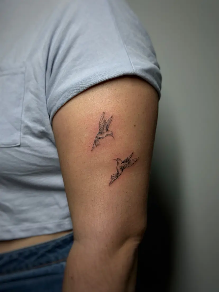 Two small fine-line birds tattoo on an upper arm