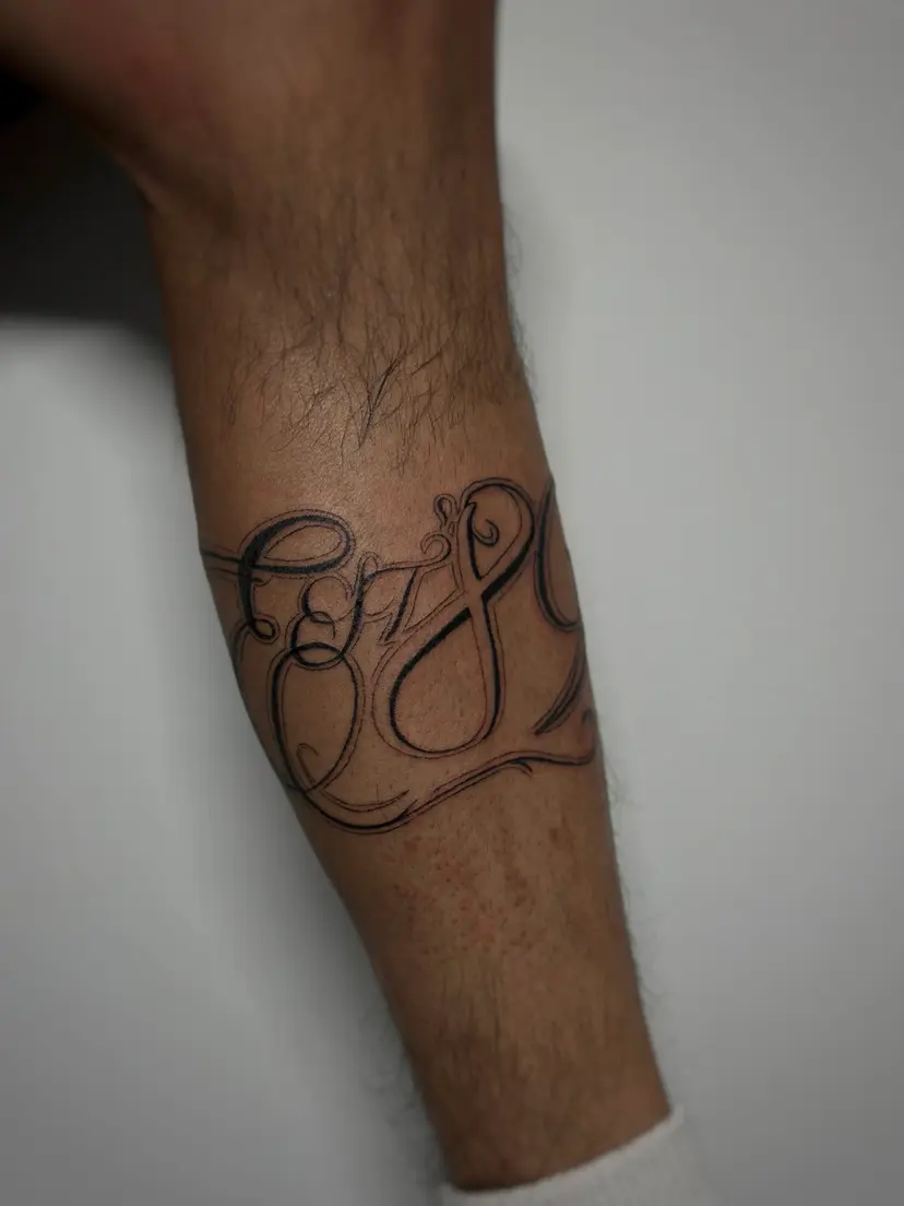 Ornate script lettering tattoo on a forearm