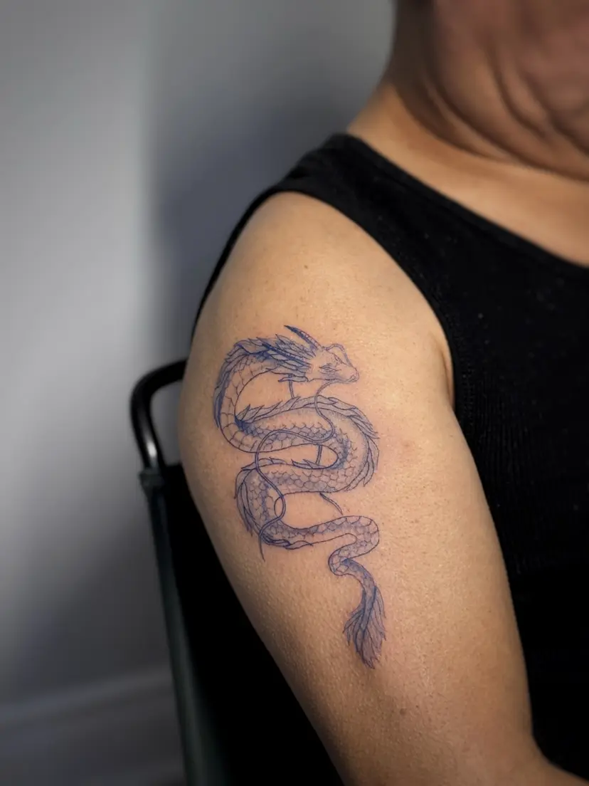 Fine-line dragon tattoo on an upper arm