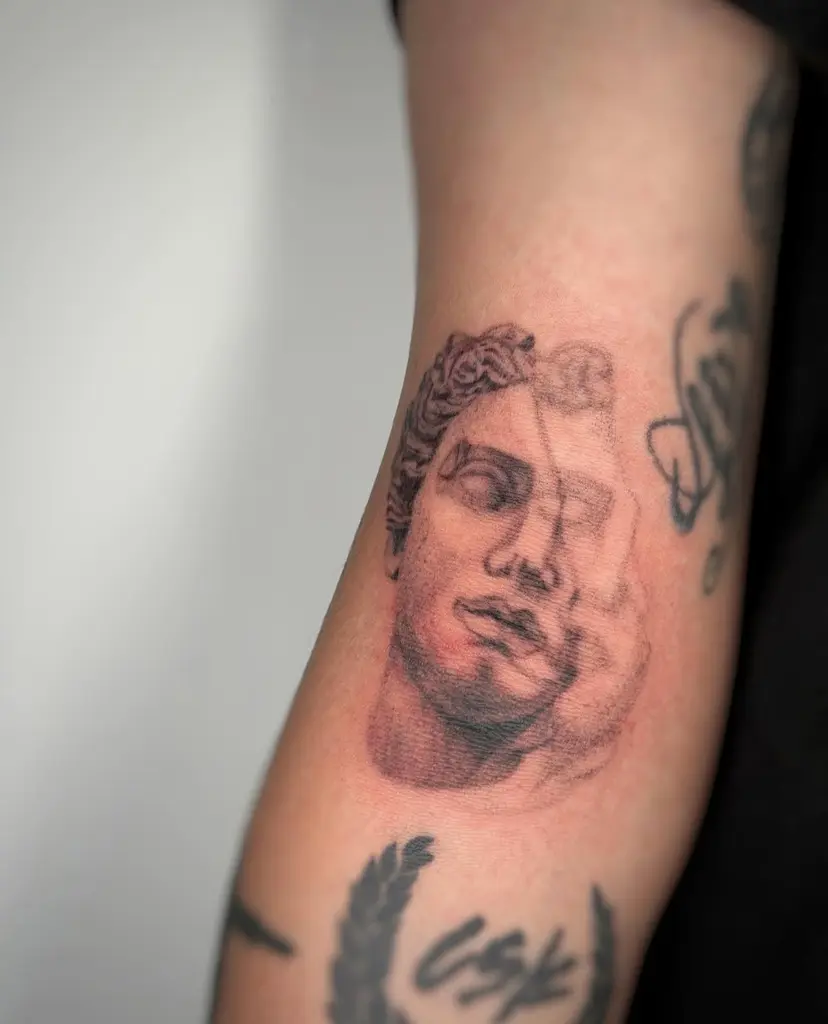 Black and grey statue face tattoo on an arm